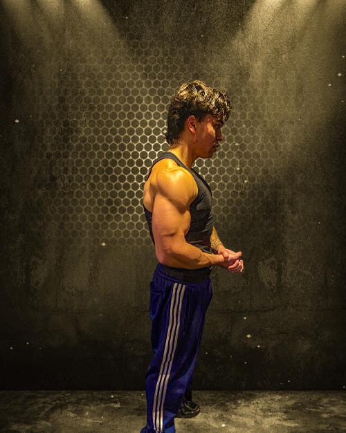 Auteur model Dylan - Portretfoto van mij in een tanktop, met zichtbare spieren, voor een zwarte muur met textuur en belichting die op mij ger